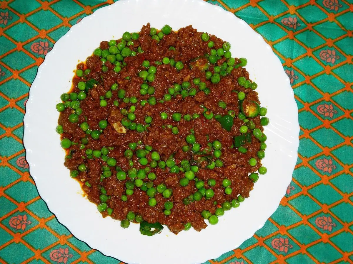 Carne picada especiada con guisantes en un plato blanco sobre mantel colorido