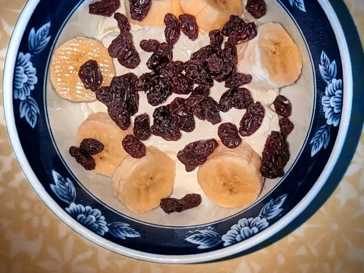 Cuenco azul de yogur con rodajas de plátano y pasas visto desde arriba
