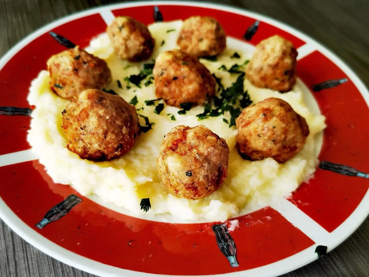 Albóndigas doradas sobre puré cremoso con hierbas picadas en un plato blanco con borde rojo