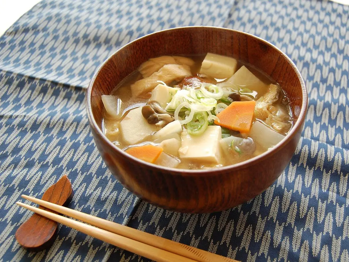 Cuenco de madera con sopa de tofu, zanahoria, rábano y cebolleta