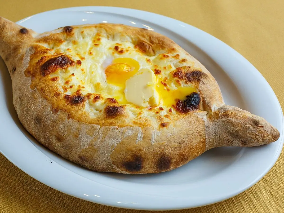 Khachapuri adjaruli, barca de pan rellena de queso fundido con yema de huevo en un plato blanco