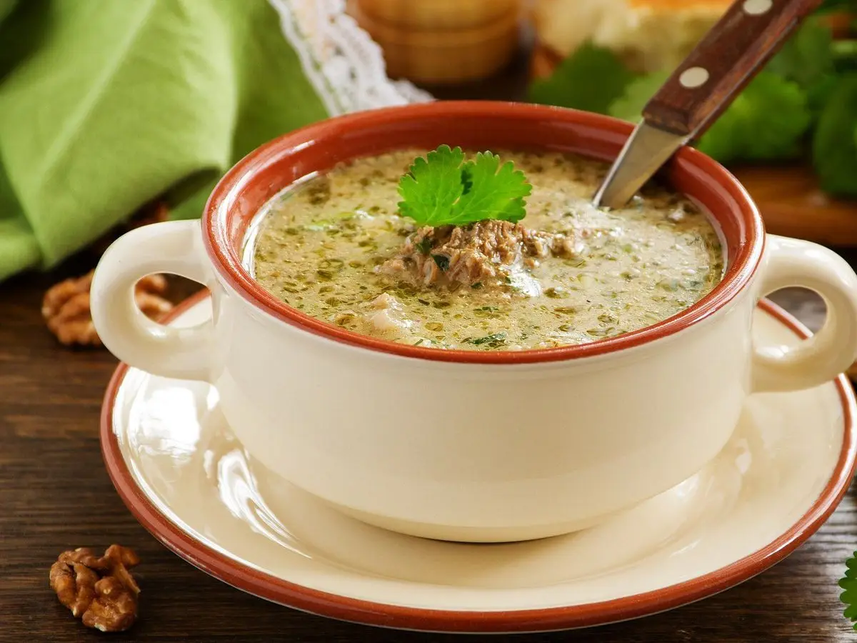 Taza de sopa georgiana de ternera y arroz con cilantro, rodeada de nueces y hierbas frescas