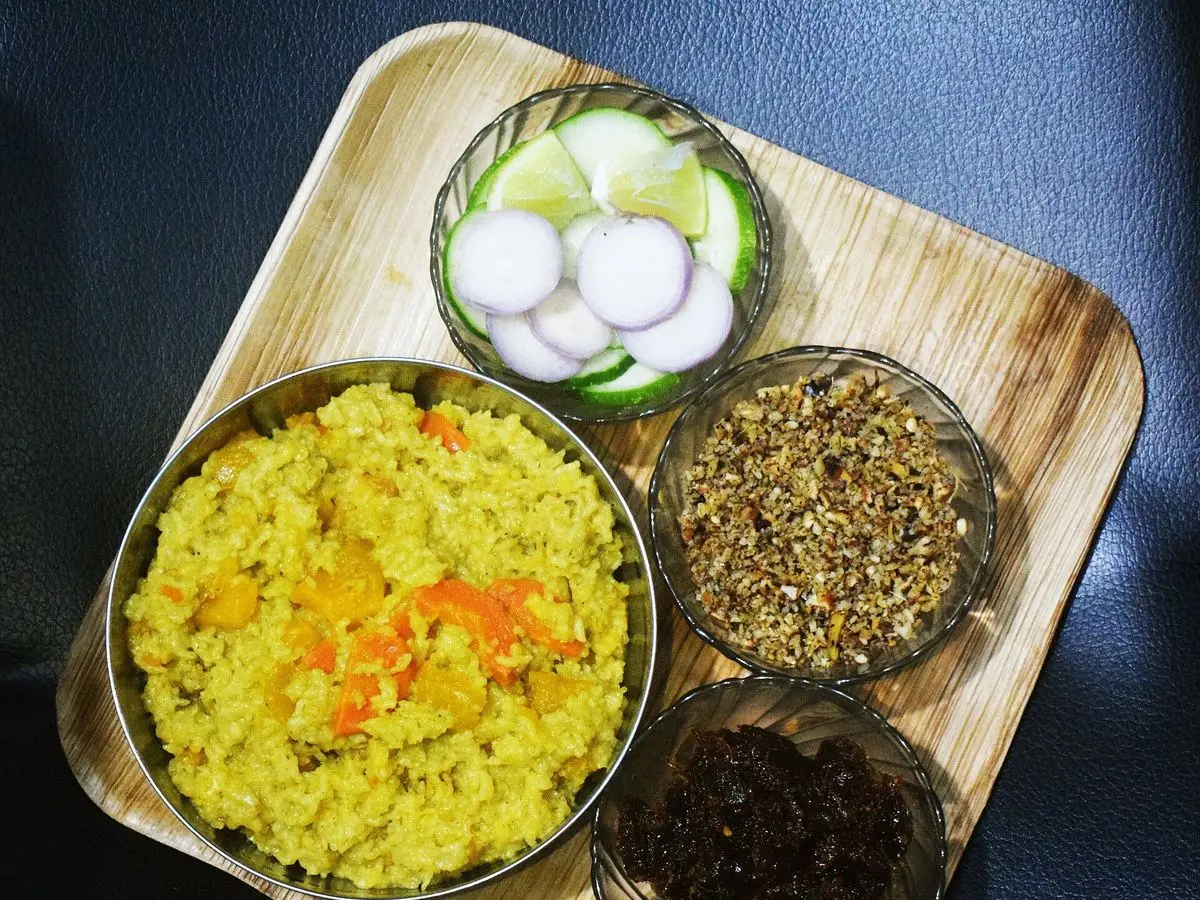 Cuenco de khichdi amarillo de arroz y legumbre con zanahoria, junto a pequeños cuencos de acompañamiento