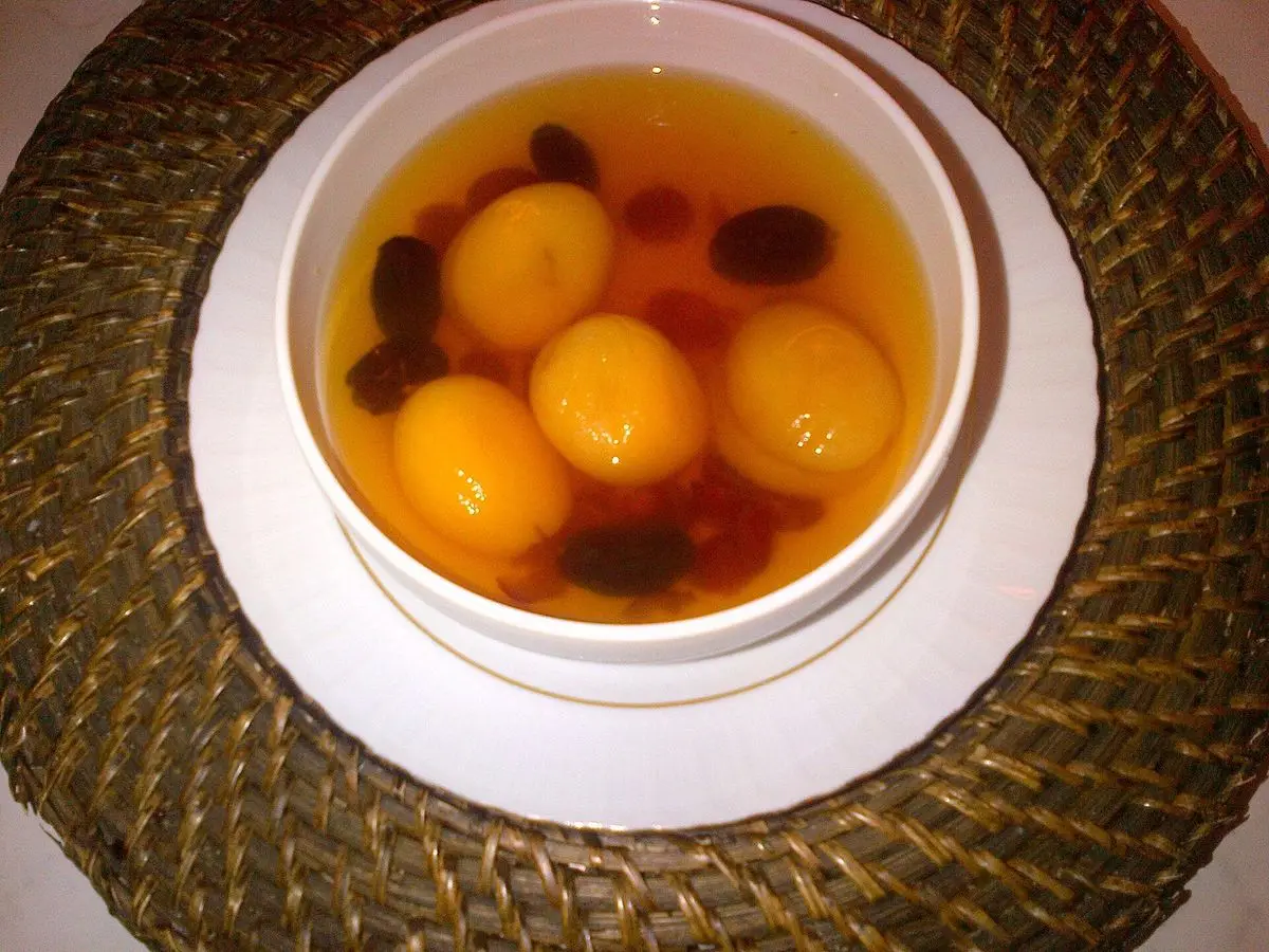 Cuenco con compota de orejones, ciruelas pasas y uvas pasas en almíbar sobre un plato blanco