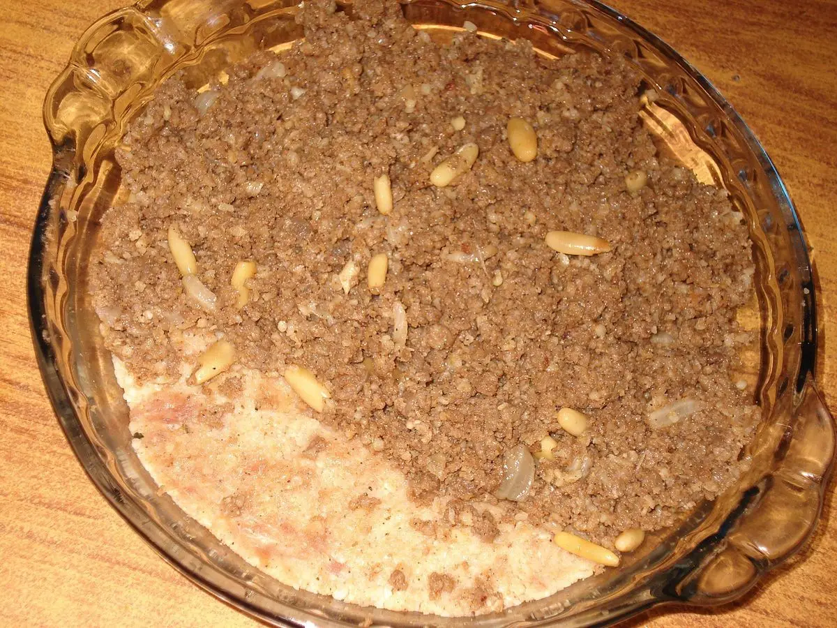 Kibbeh al horno en fuente de cristal con cobertura de carne y piñones