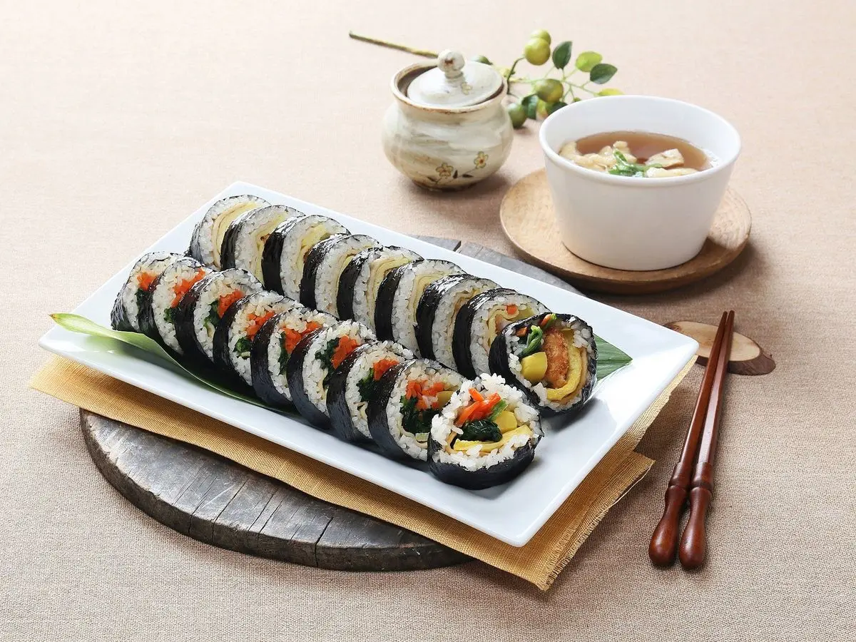 Rollos de kimbap cortados en rodajas sobre una bandeja blanca con un cuenco de sopa