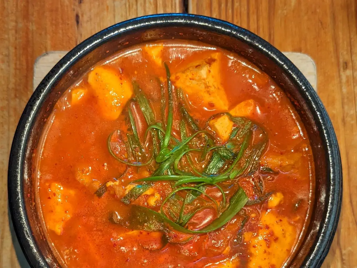 Cazuela de guiso rojo de kimchi con tofu y cebolleta picada