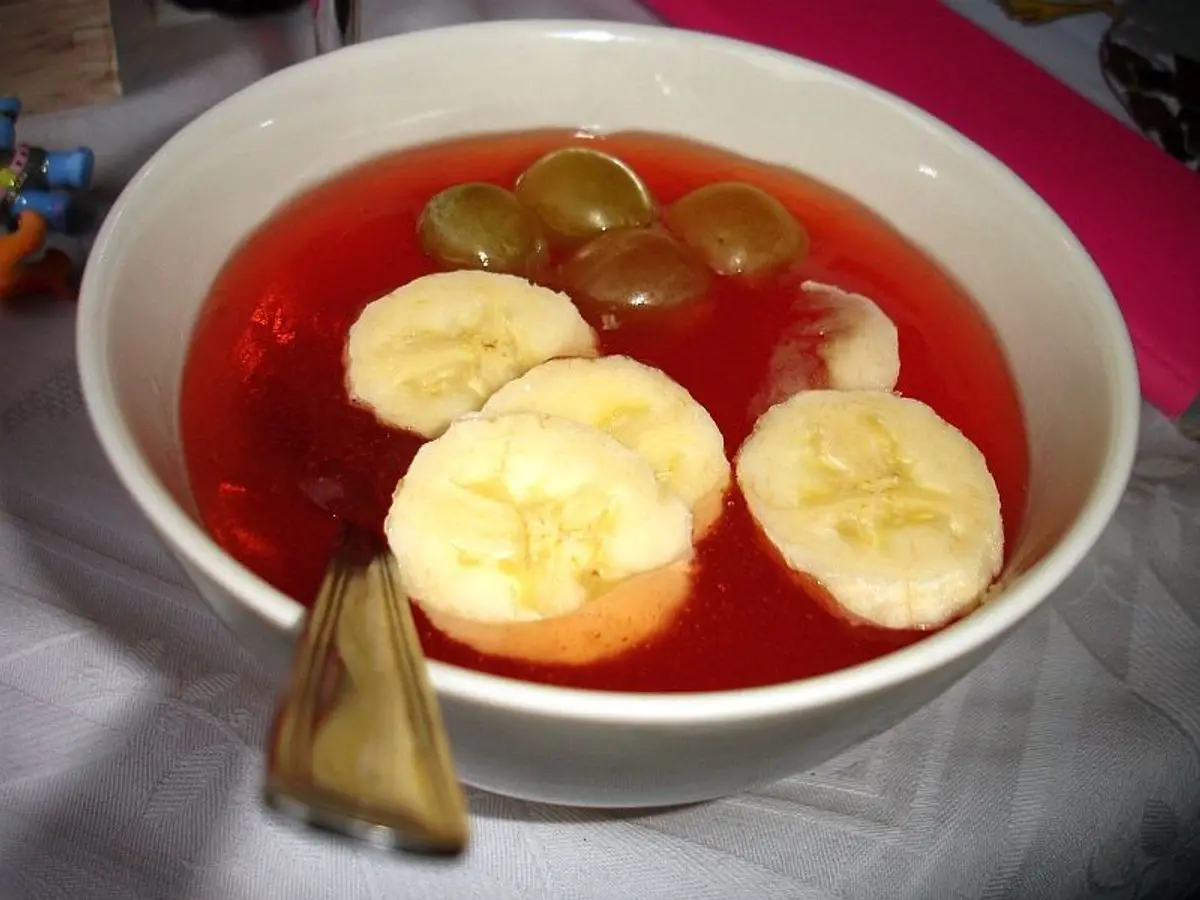 Cuenco de kissel rojo, crema espesa de frutos, con rodajas de plátano y uvas