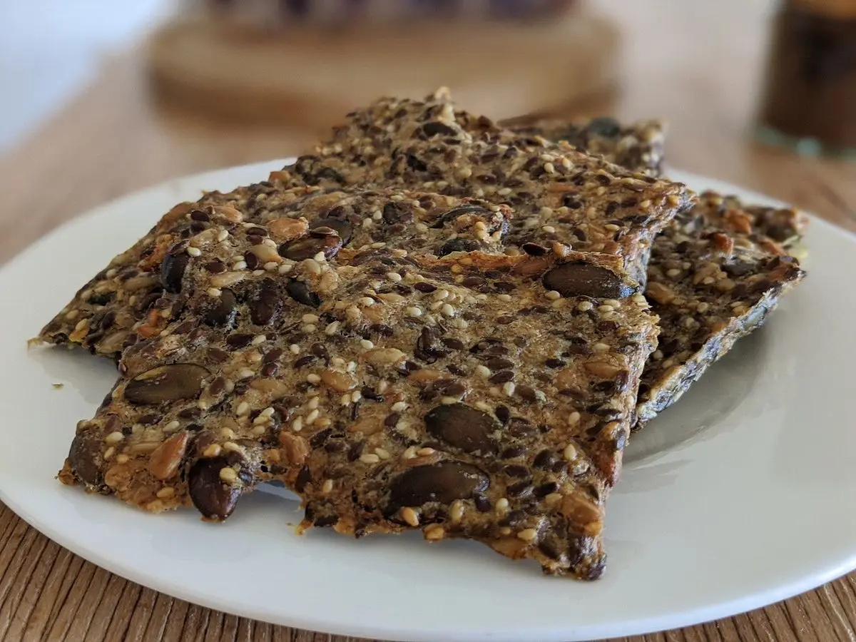 Pan crujiente sueco de semillas y cereales troceado en un plato blanco sobre una mesa de madera