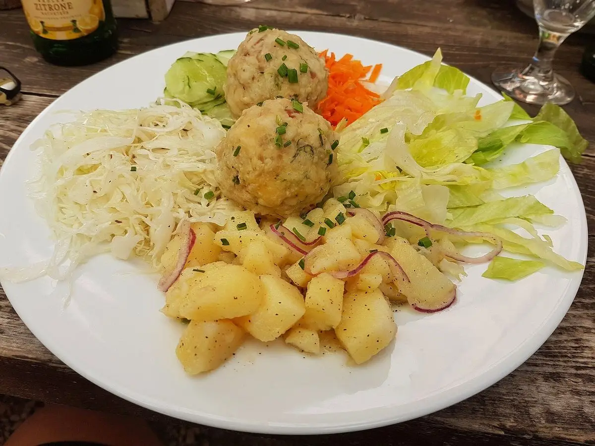 Albóndigas de pan con panceta con ensalada de col, lechuga y patatas salteadas en un plato blanco