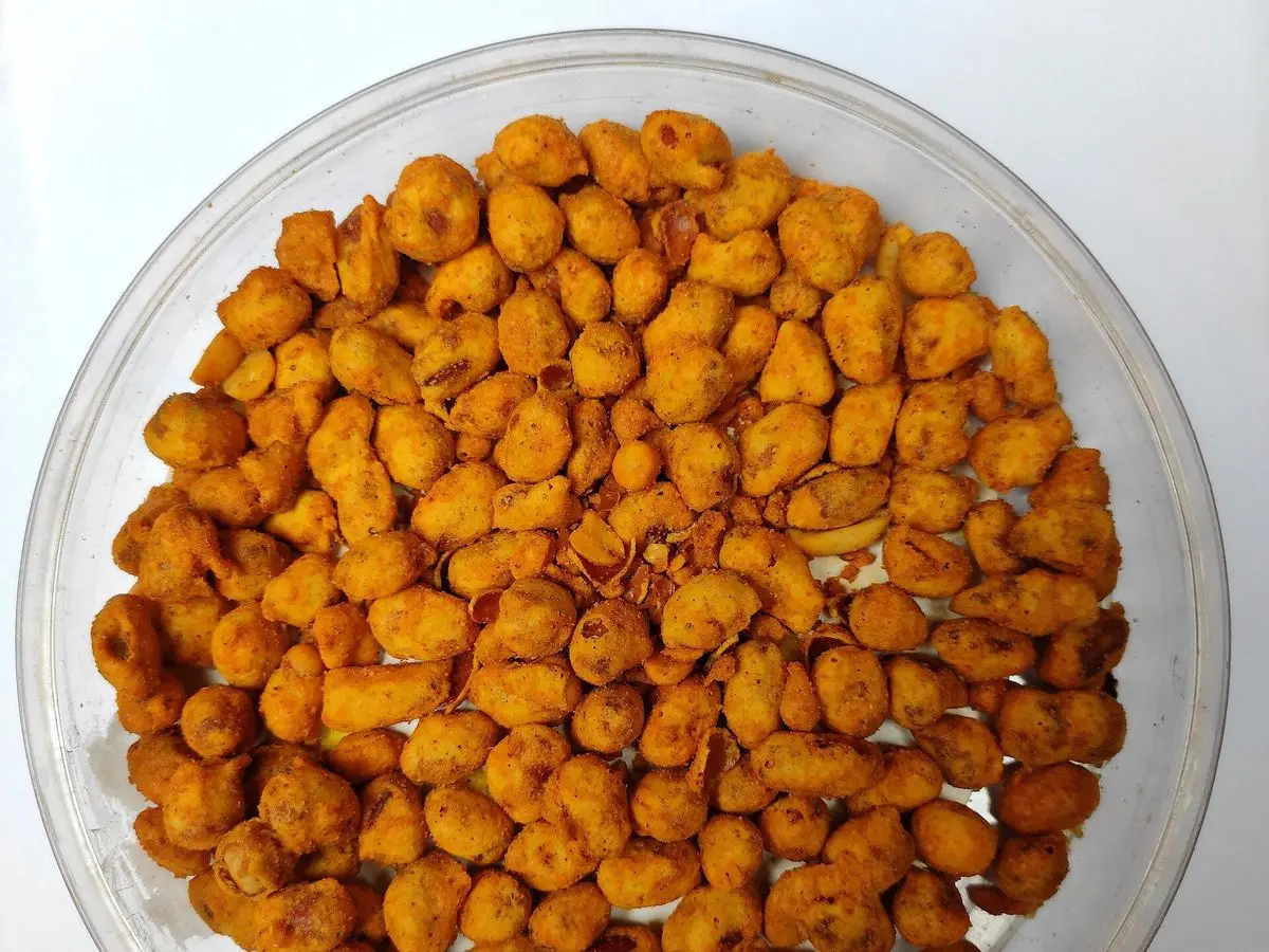Cuenco de cristal con cacahuetes tostados y especiados de color anaranjado, picoteo seco