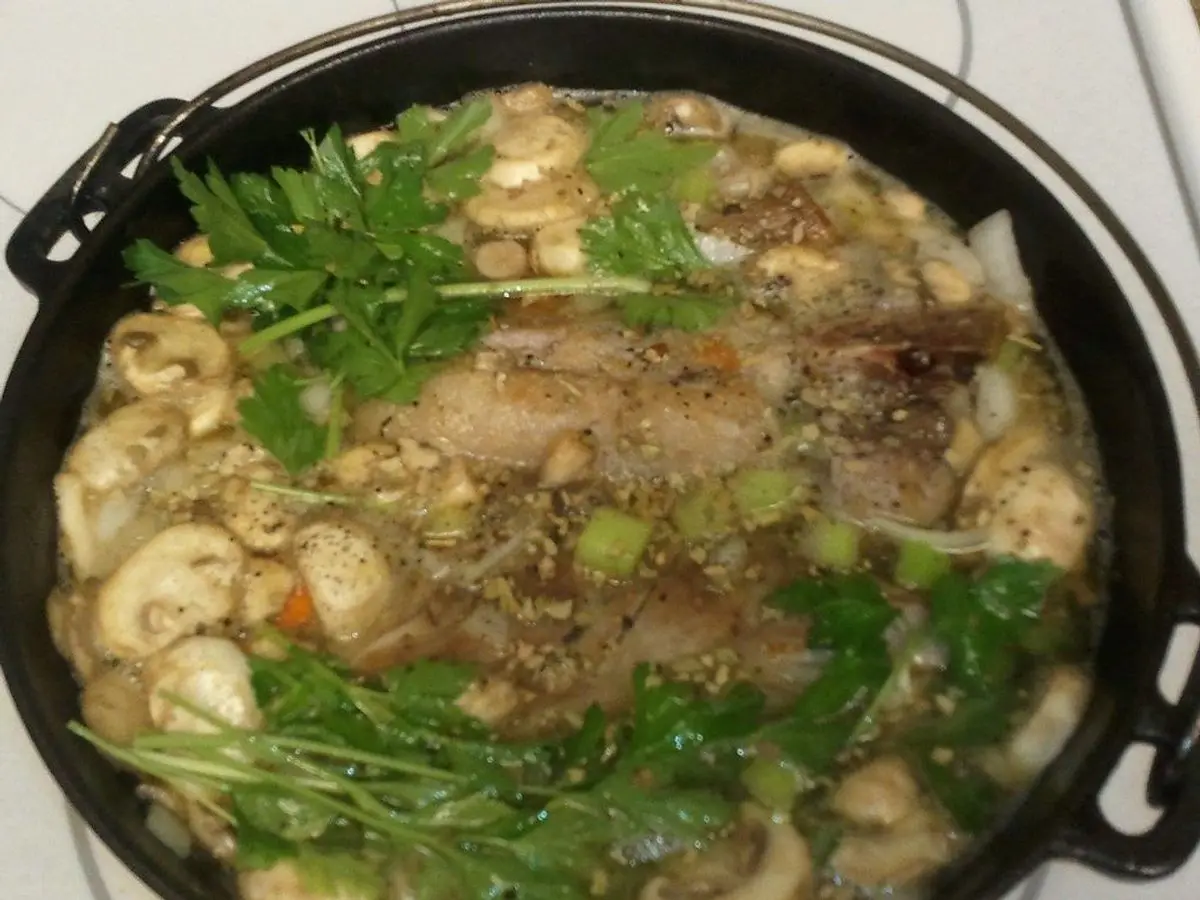 Olla negra con guiso de cerdo, setas y verduras con hierbas frescas por encima