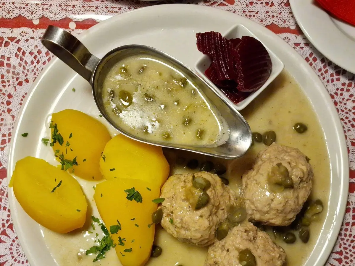 Albóndigas en salsa blanca con alcaparras, patatas cocidas y remolacha en un plato blanco