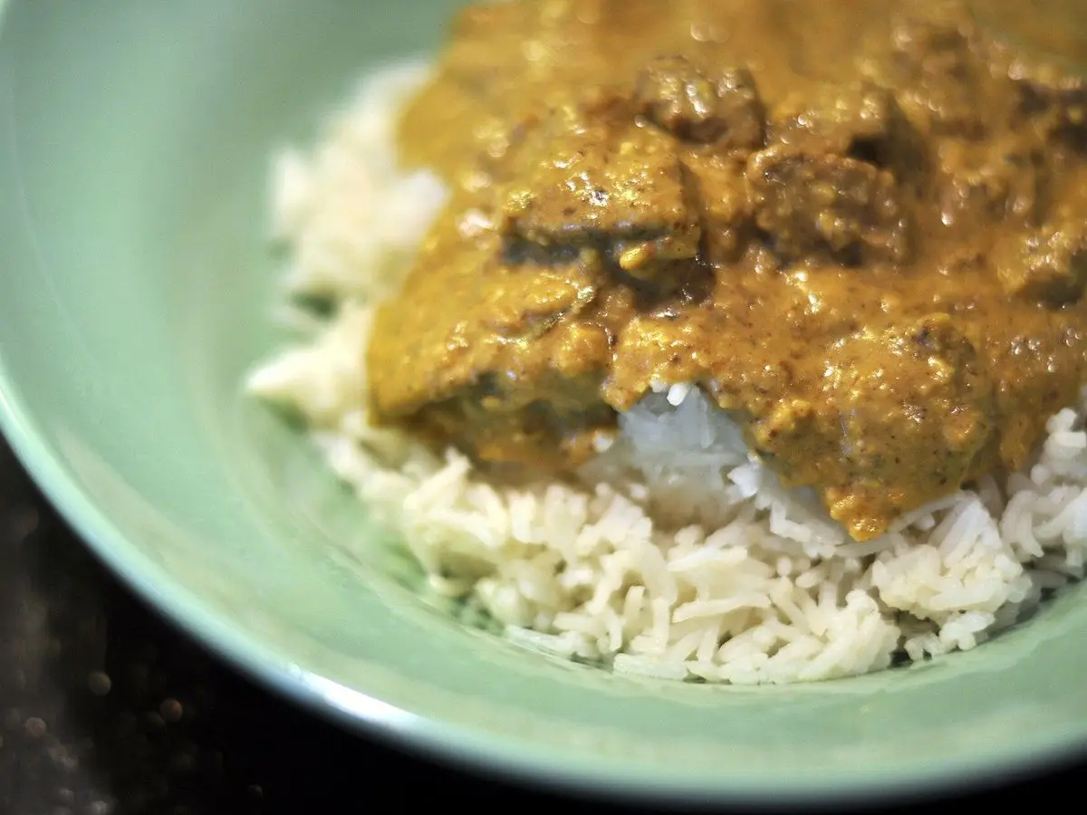 Cuenco verde con korma de cordero en salsa cremosa sobre arroz basmati
