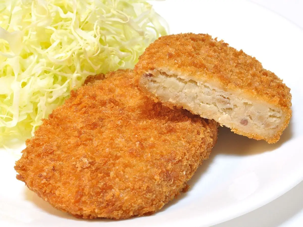 Croquetas japonesas empanadas con panko, una abierta, junto a col blanca finamente cortada en un plato