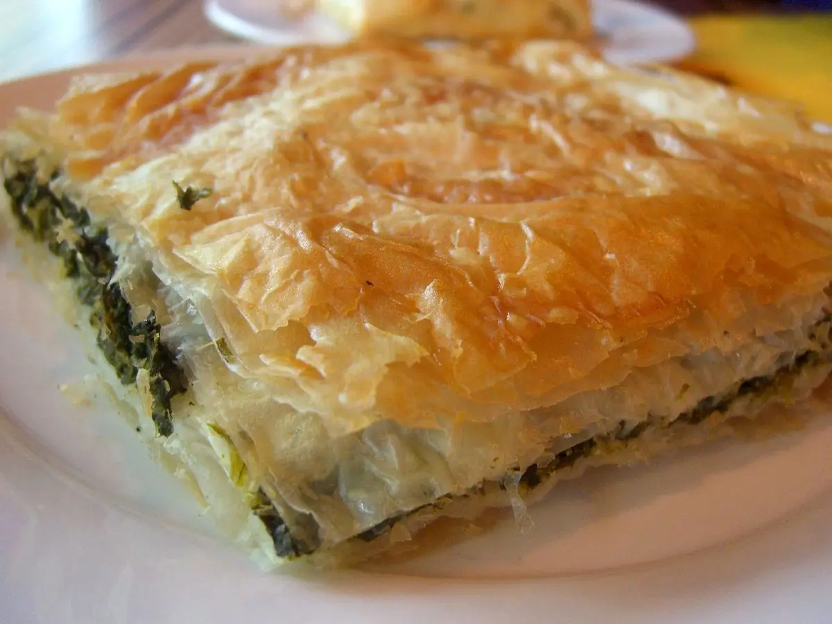 Porción de pastel salado de masa filo crujiente con relleno de verdura verde en un plato