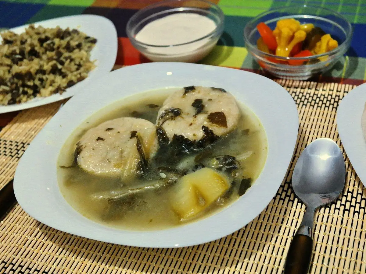 Plato hondo de sopa con albóndigas de sémola, hojas de acelga y patata, con encurtidos y tahini al lado