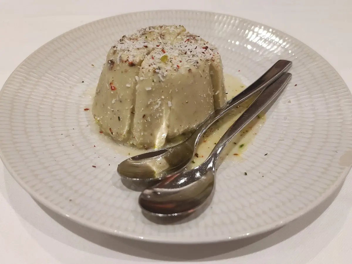 Kulfi de pistacho desmoldado sobre un plato blanco con dos cucharas