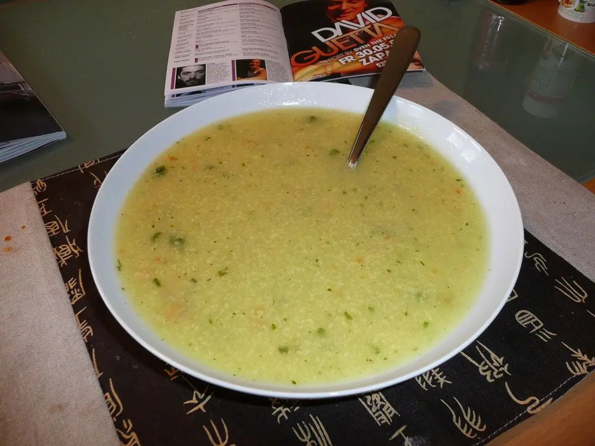 Plato hondo blanco de sopa espesa amarillenta con cuchara sobre un salvamantel