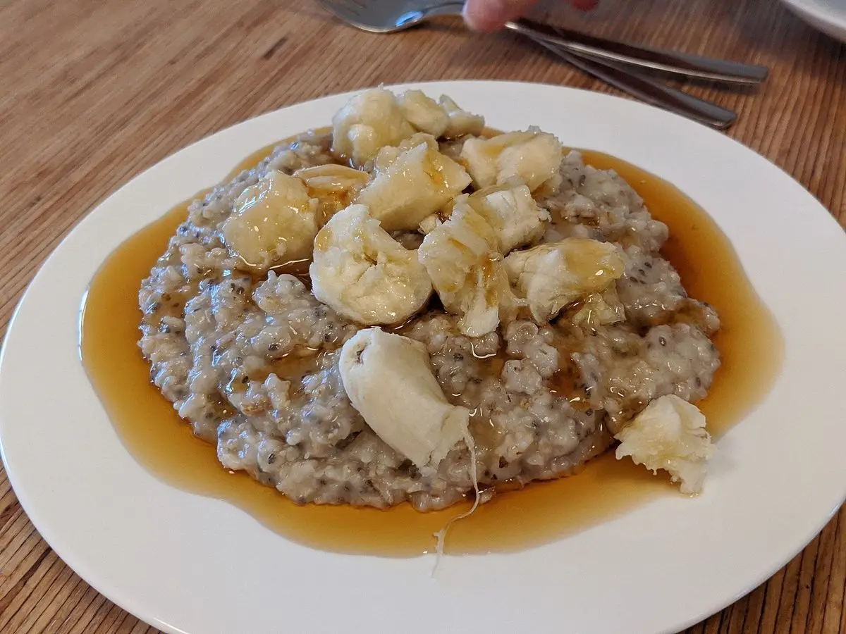 Plato de gachas espesas de avena con trozos de plátano y un chorro de almíbar sobre una mesa de madera
