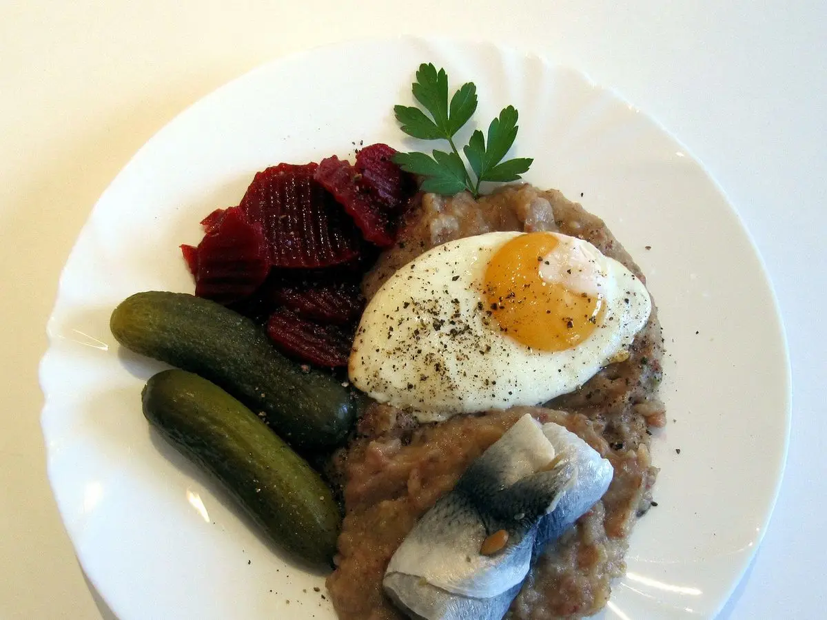 Labskaus con huevo frito, arenque, remolacha y pepinillos en un plato blanco
