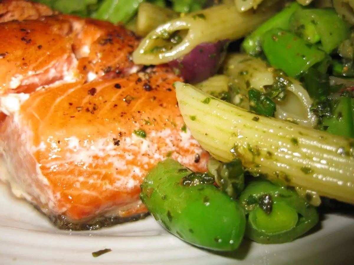 Lomo de salmón a la plancha con pasta y guisantes tirabeques en un plato blanco