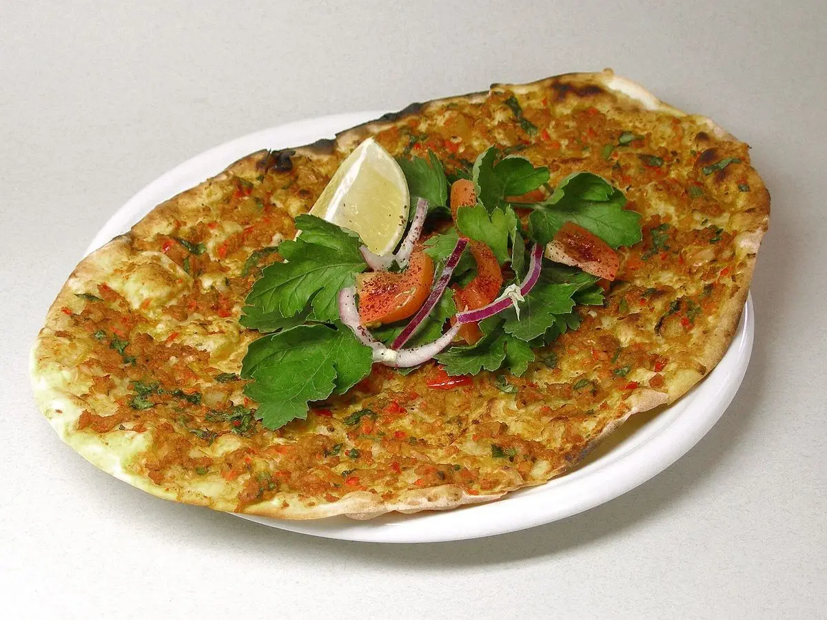 Lahmacun de carne picada con ensalada de tomate, cebolla y perejil y un trozo de limón