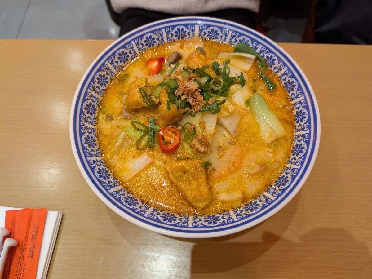 Cuenco decorado de sopa laksa anaranjada con fideos, verduras verdes y guindilla roja visto desde arriba