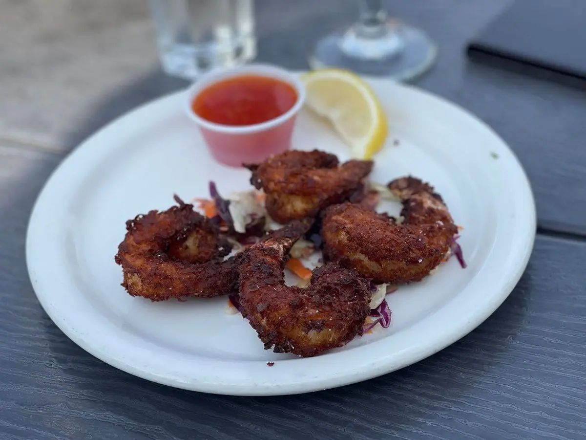 Langostinos rebozados en coco dorados en un plato blanco con salsa roja y una rodaja de limón