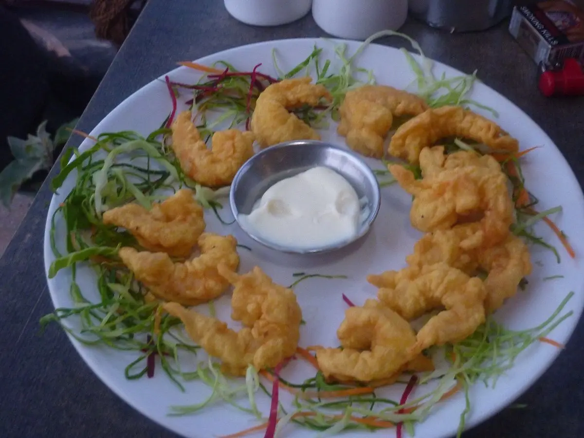 Langostinos rebozados dorados con un cuenco de salsa blanca en un plato con hilos de verdura