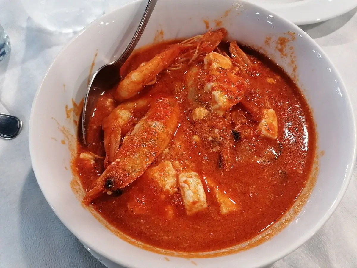 Cuenco blanco de gambas en salsa de tomate roja con trozos de queso feta