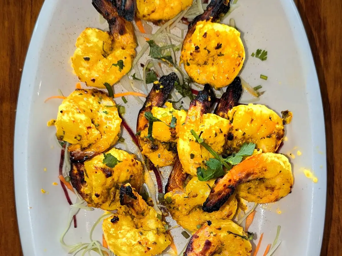 Langostinos tandoori amarillos a la plancha en un plato blanco con salsa verde de menta