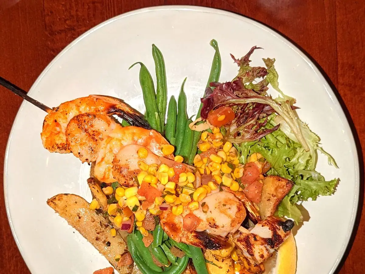 Plato de gambas y vieiras a la plancha con maíz, judías verdes, patata y hojas de ensalada