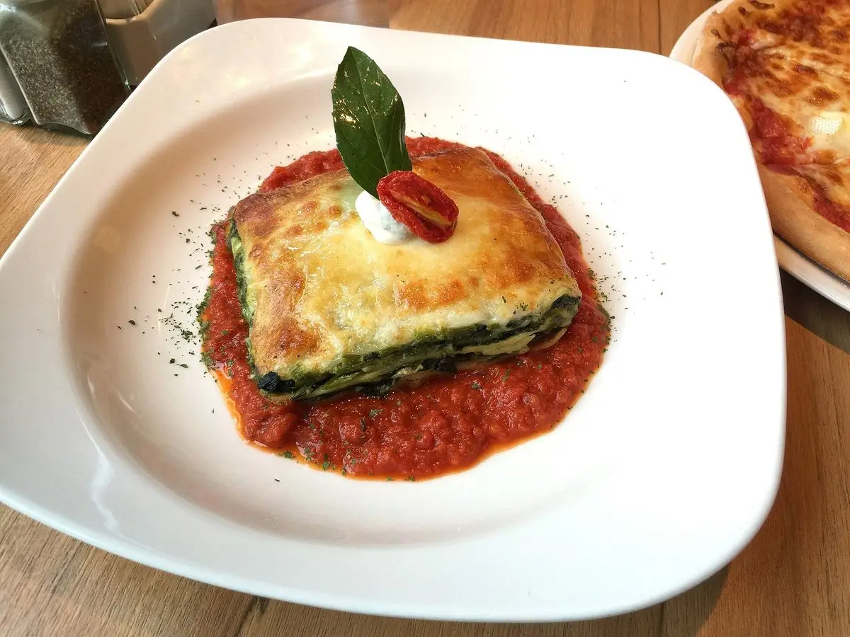Porción de lasaña de espinacas y ricotta sobre salsa de tomate en un plato blanco con albahaca