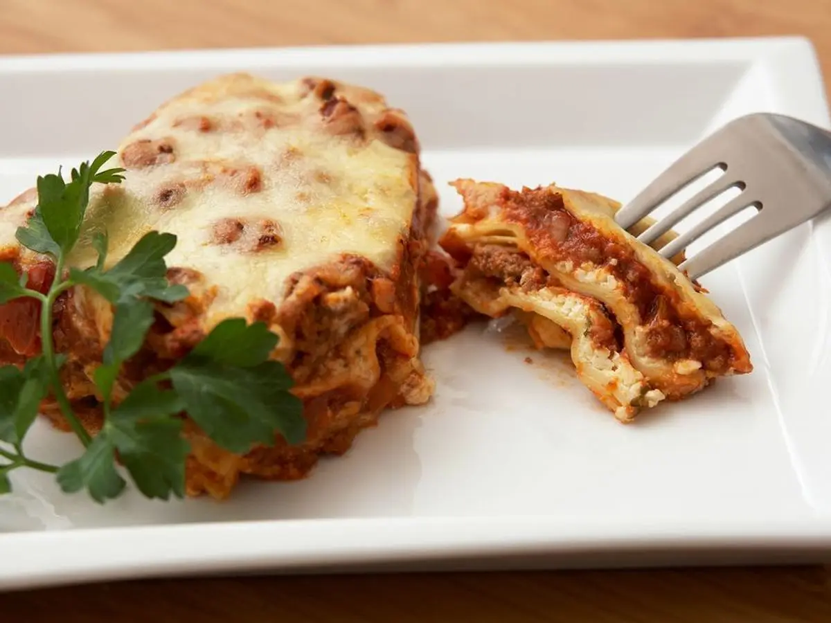Porción de lasaña de carne gratinada con queso en un plato blanco con tenedor