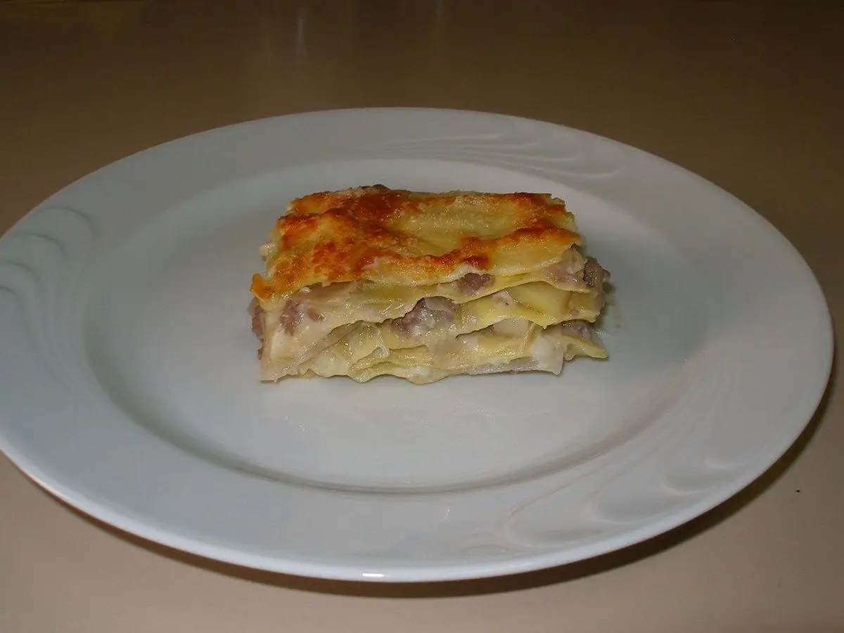 Porción de lasaña blanca gratinada con bechamel en un plato blanco