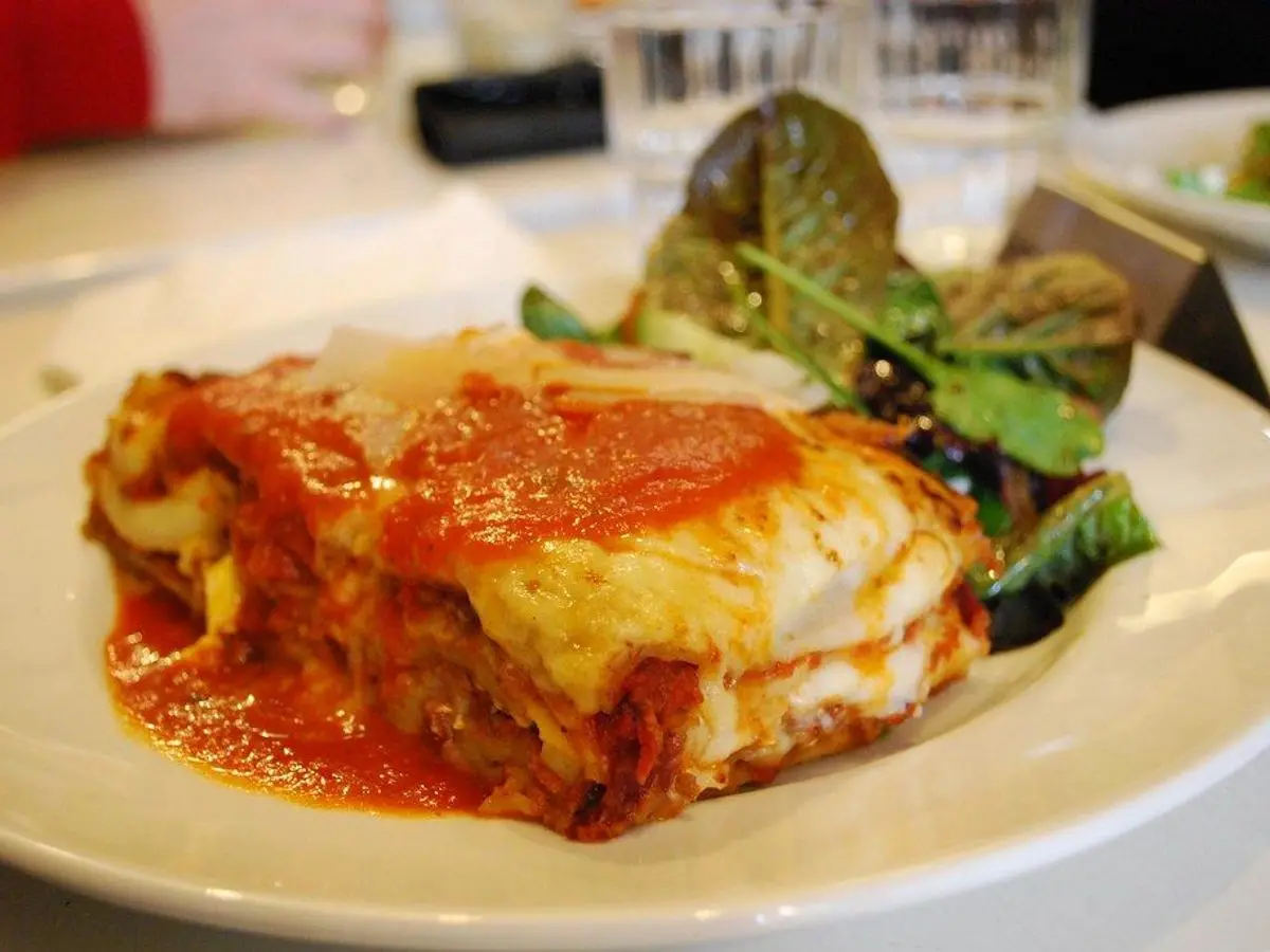 Ración de lasaña gratinada con salsa de tomate y ensalada en un plato blanco