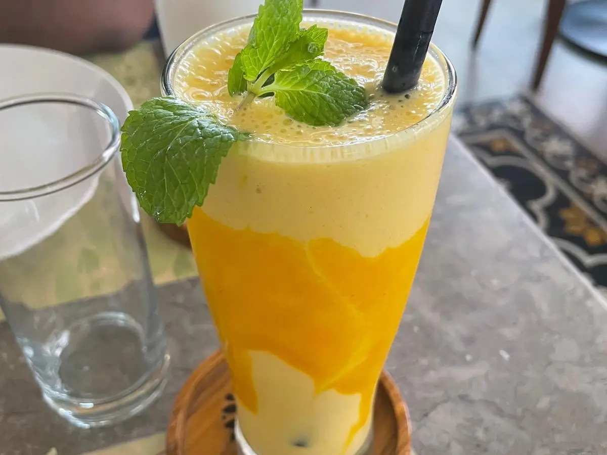 Batido cremoso de mango en un vaso alto con hojas de menta y pajita negra