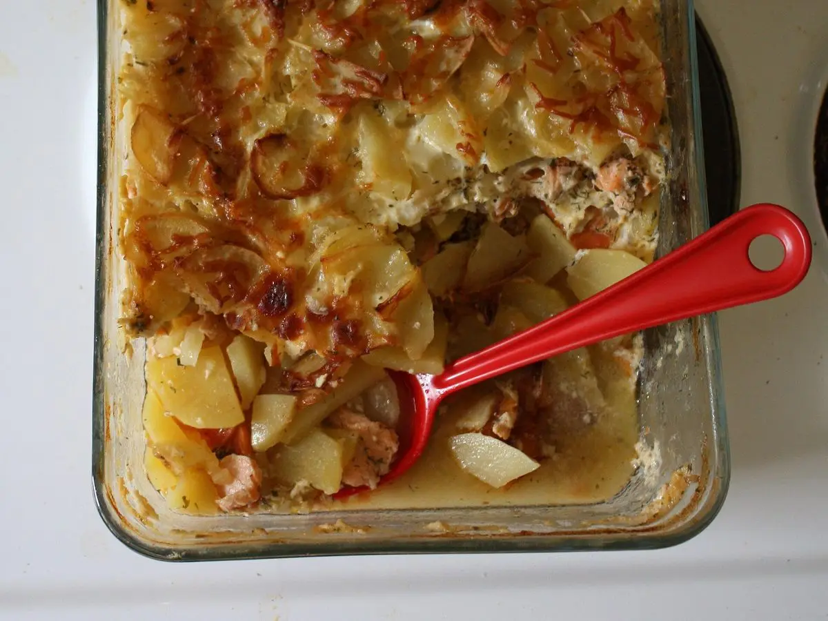 Fuente de horno con gratinado dorado de patata en láminas y salmón, con una cuchara roja