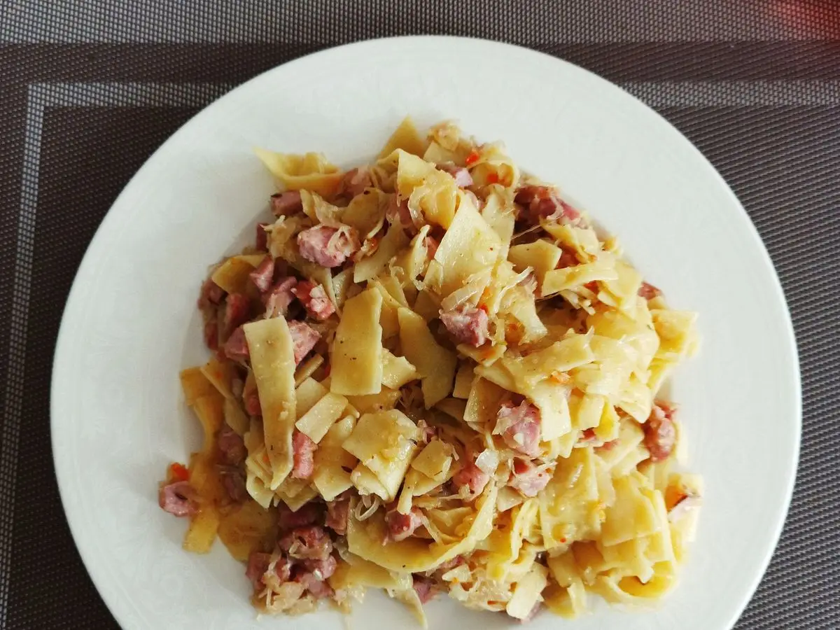 Pasta cuadrada salteada con col y trozos de salchicha en un plato blanco