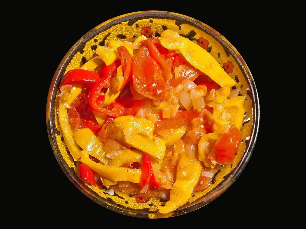Cuenco de lecsó de pimientos amarillos y rojos con tomate sobre fondo negro