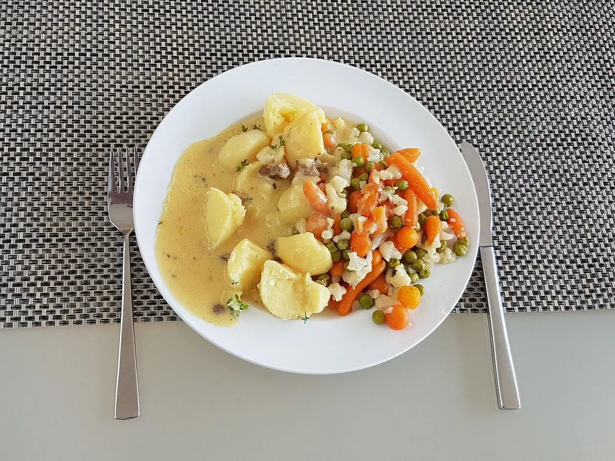 Menestra de verduras con zanahoria, espárragos y patatas en salsa holandesa en un plato blanco