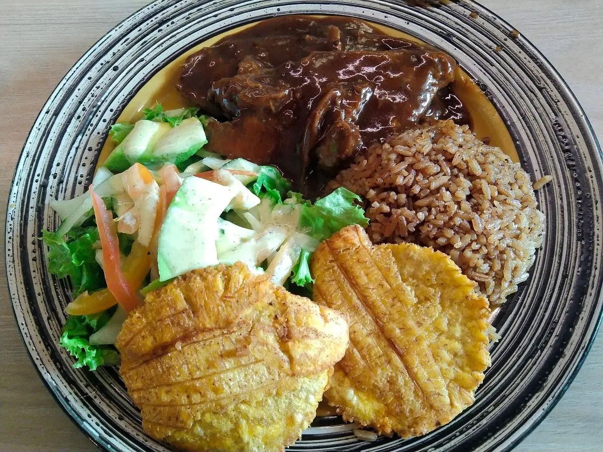 Lengua guisada en salsa oscura con ensalada, arroz y plátano frito en un plato
