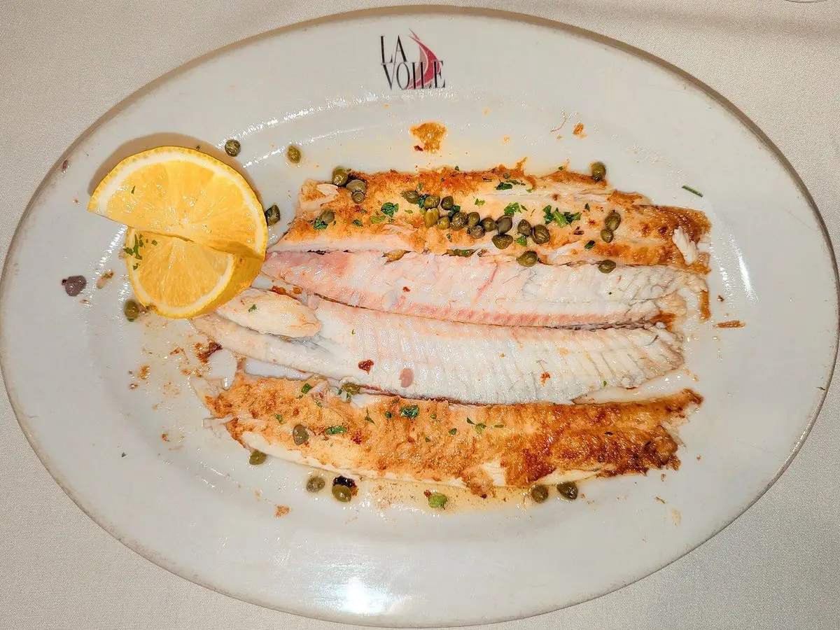 Lenguado a la plancha con alcaparras y gajo de limón servido en una fuente ovalada blanca