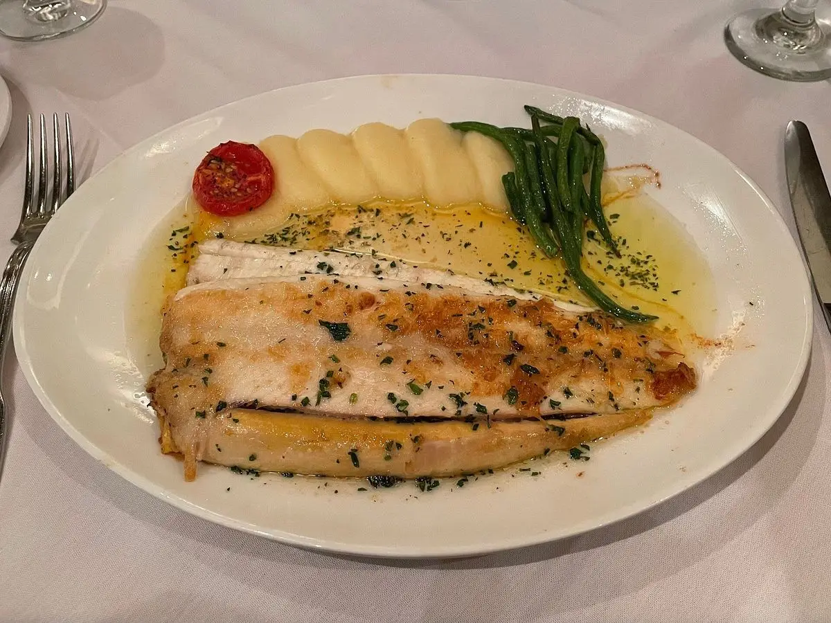 Lenguado en salsa de mantequilla con patatas cocidas, judías verdes y un tomate cherry en un plato blanco