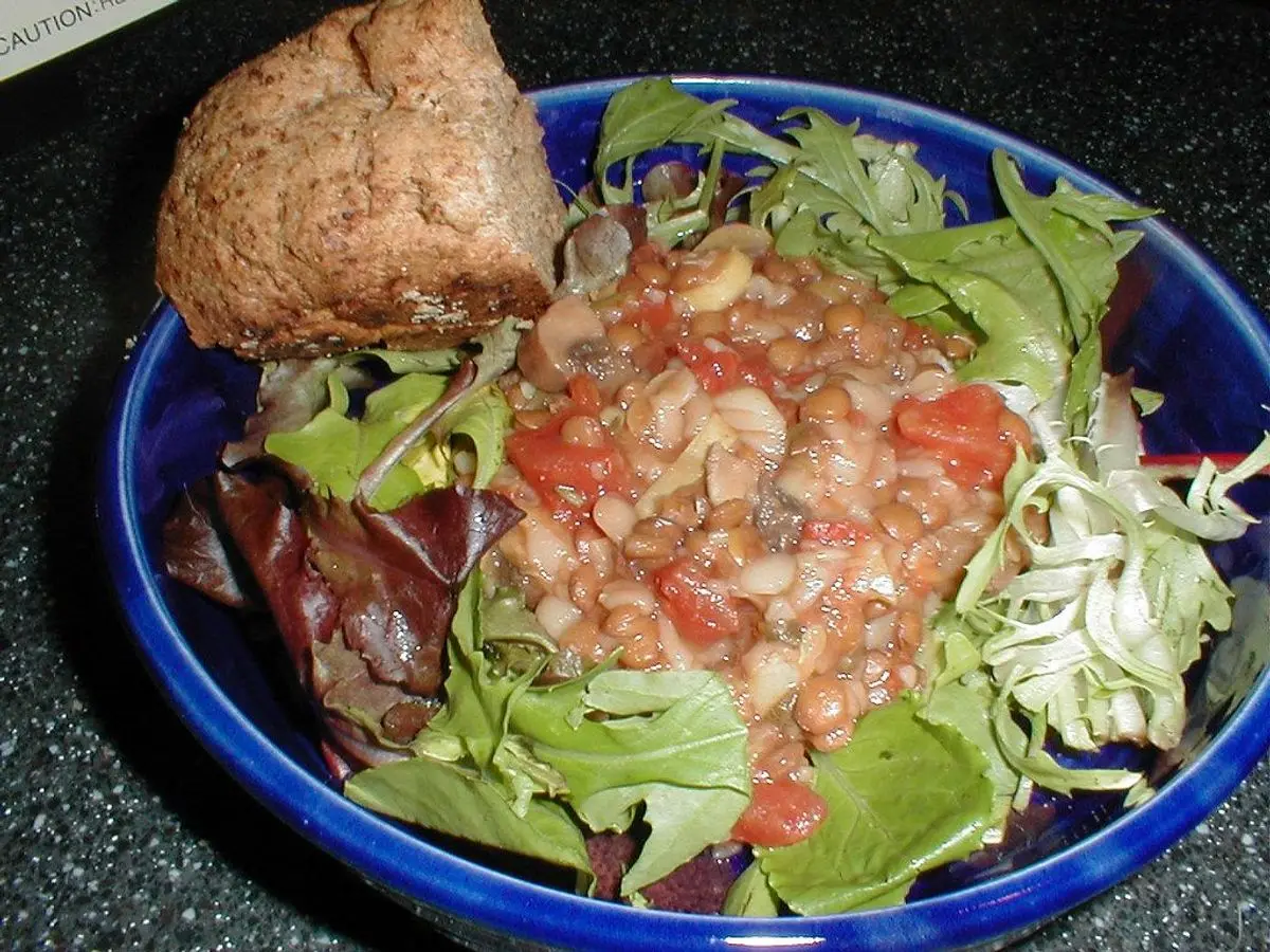 Cuenco azul con lentejas y tomate sobre hojas verdes y un trozo de pan