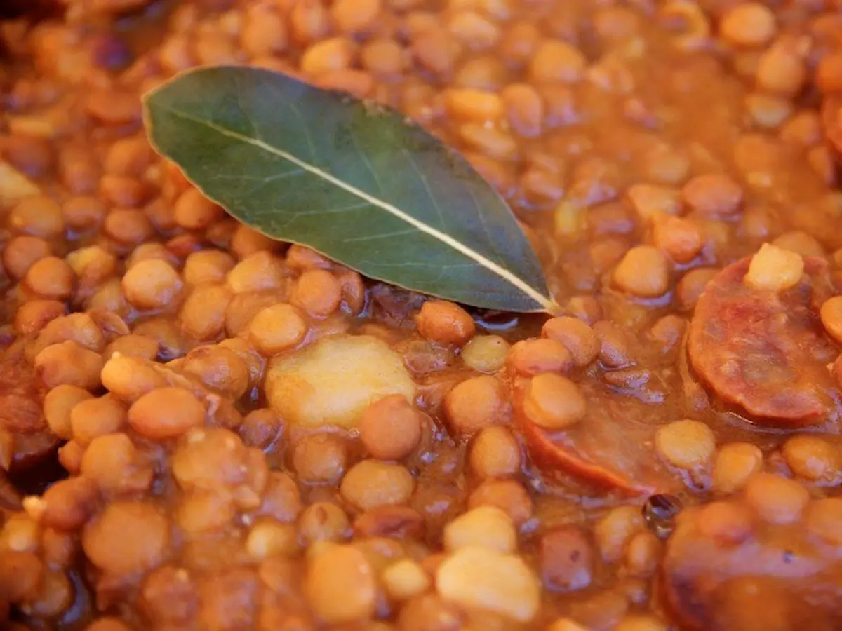 Primer plano de lentejas guisadas con rodajas de chorizo y una hoja de laurel