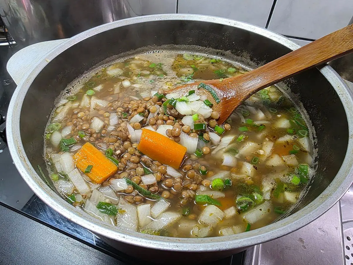 Olla con guiso de lentejas, zanahoria y verduras troceadas con cuchara de madera