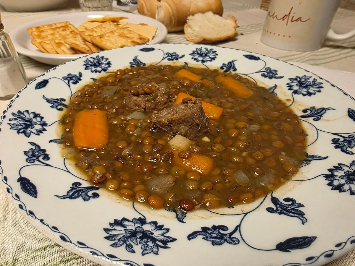 Plato de lentejas estofadas con zanahoria sobre un mantel, con pan al fondo