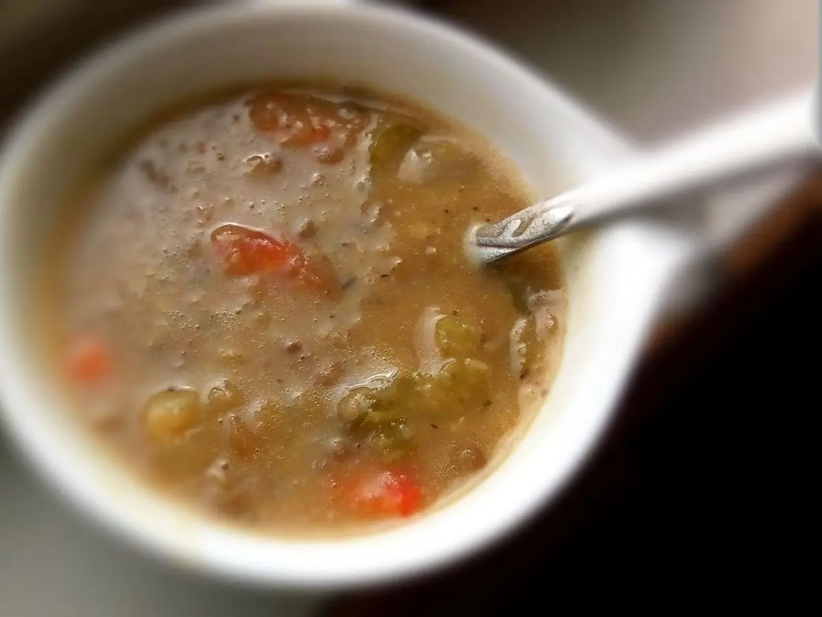 Cuenco blanco de guiso de lentejas con verduras y una cuchara